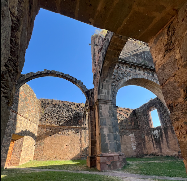 Nombrado Pueblo Mágico desde 2015, Mascota, Jalisco, cautiva a quienes lo visitan con su aire puro, sus paisajes encantadores y su fascinante historia. Entre sus numerosos atractivos destaca la Iglesia Inconclusa de La Preciosa Sangre de Cristo. Ubicado en el corazón del pueblo, en las calles Libertad y Rosa Dávalos, este imponente lugar, con sus arcos majestuosos y estructuras incompletas, transporta a los visitantes al siglo XIX. El templo fue concebido en 1896 para ser el Santuario de la Virgen de Talpa y las obras, realizadas completamente a mano, avanzaron hasta 1904 cuando los movimientos pre-revolucionarios que estallaron en 1905 dificultaron su culminación. En 1908, el gobierno incautó los bienes destinados a su construcción para financiar la guerra, interrumpiendo los trabajos y posteriormente, en 1926, el lugar fue tomado por los cristeros durante el conflicto religioso, y las paredes incompletas se convirtieron en escenarios de encarcelamientos y fusilamientos. Tras esos oscuros episodios, la construcción quedó abandonada y en 1945, el templo fue declarado patrimonio nacional, lo que aseguró su preservación como una reliquia histórica. Hoy, sus arcos y torres inacabadas permanecen como un testimonio del pasado, inmortalizadas en el tiempo. Actualmente, estas ruinas son uno de los puntos más visitados de Mascota, su imponente arquitectura y el peso de su historia cautivan a quienes se acercan a conocerlas. Si decides visitar este mágico lugar, no olvides dejar una contribución económica al entrar, lo recaudado se destina al mantenimiento del sitio, para que las generaciones futuras puedan seguir admirándolo.